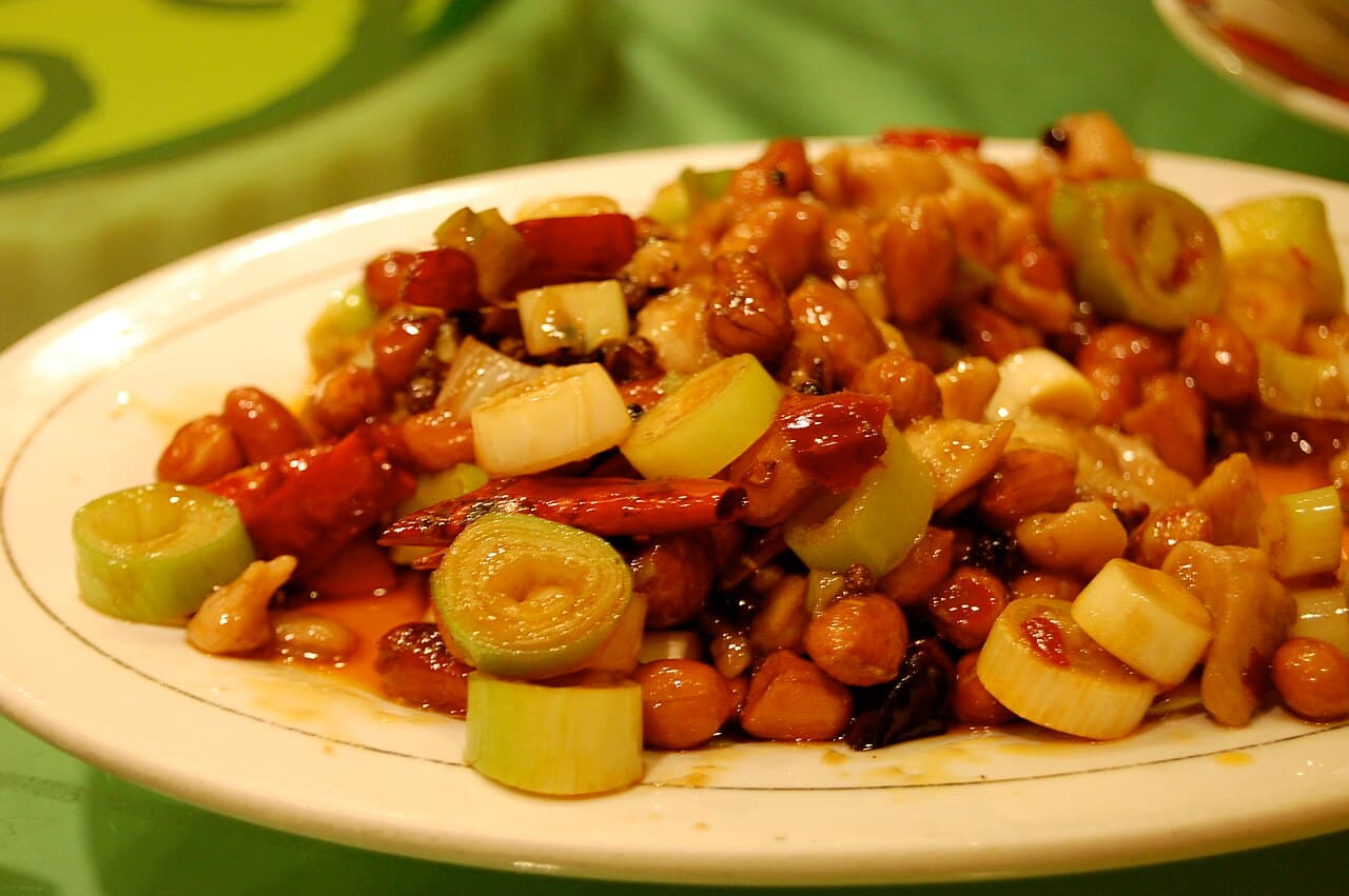 Diced chicken stir-fried with whole dried chillies, spring onion and visible peanuts on a white plate