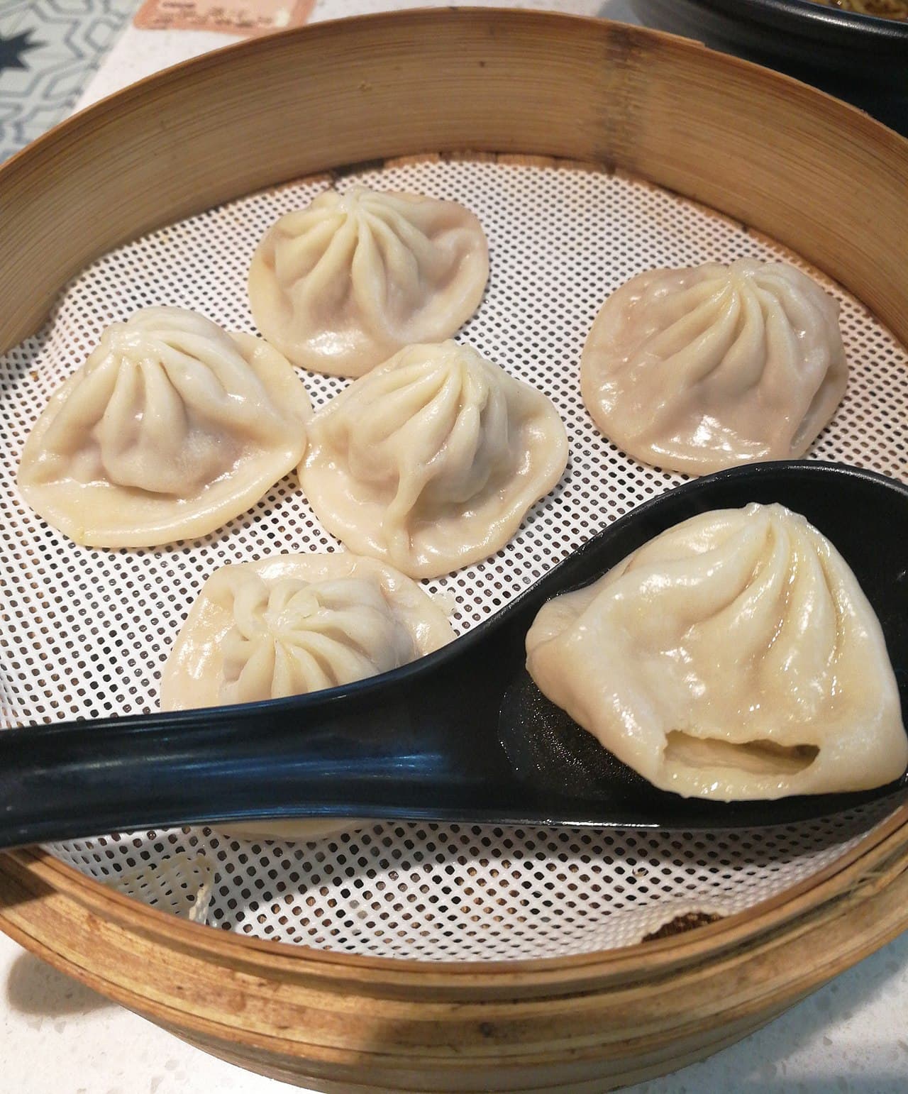 Steamed soup dumplings in a bamboo steamer with a soup spoon